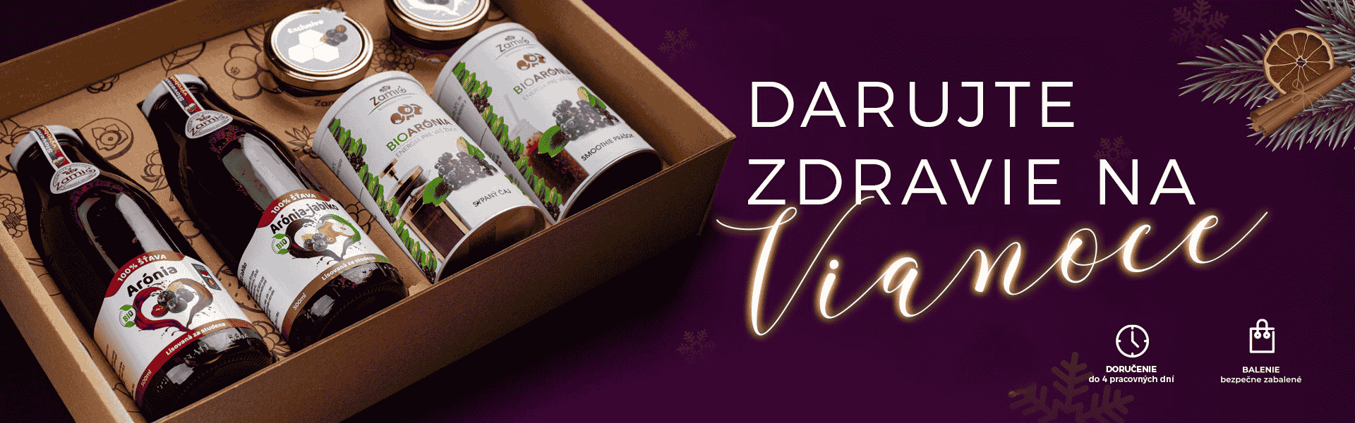 Na obrázku je znazornená na bordvom podklade Vianočná atmosféra s striebornými vetvičkami v rohu a balenie produktov z Arónie od ZAMIo To najlepšie z prírody , šťavy , džemy , sypané čaje