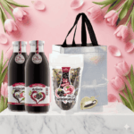 a obrazku je vo vianočnej nalade na stole položený vianočné balenie od Zamia taška , 2x fľaše sklo 100% šťava Arónia , sačok sušený caj Zamio a vrecusko s srdcom